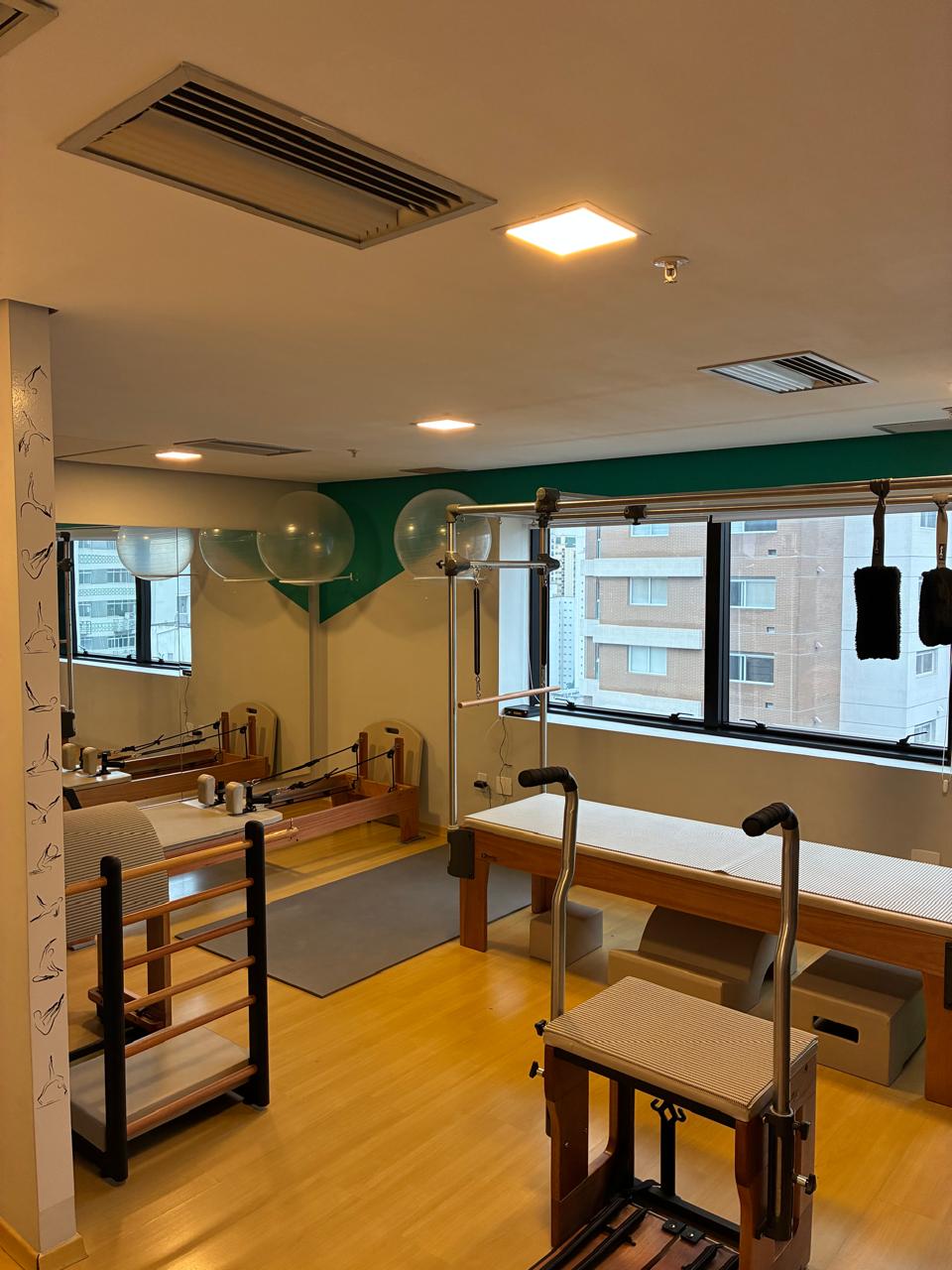 Sala do Voll Pilates Perdizes com aparelhos completos, parede verde e janelas amplas com vista da cidade